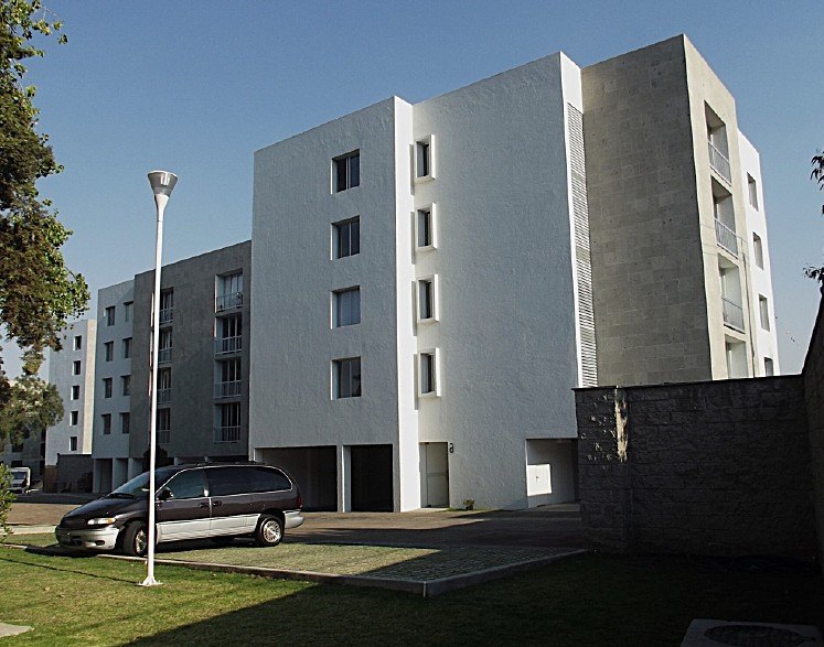 El edificio blanco en la esquina, con el estacionamiento delante